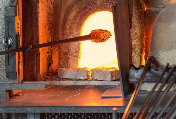 Murano glass-blowing factory. Glass blower forming beautiful piece of glass: put iron rod with attached glass object in furnace to make the glass malleable. Italy